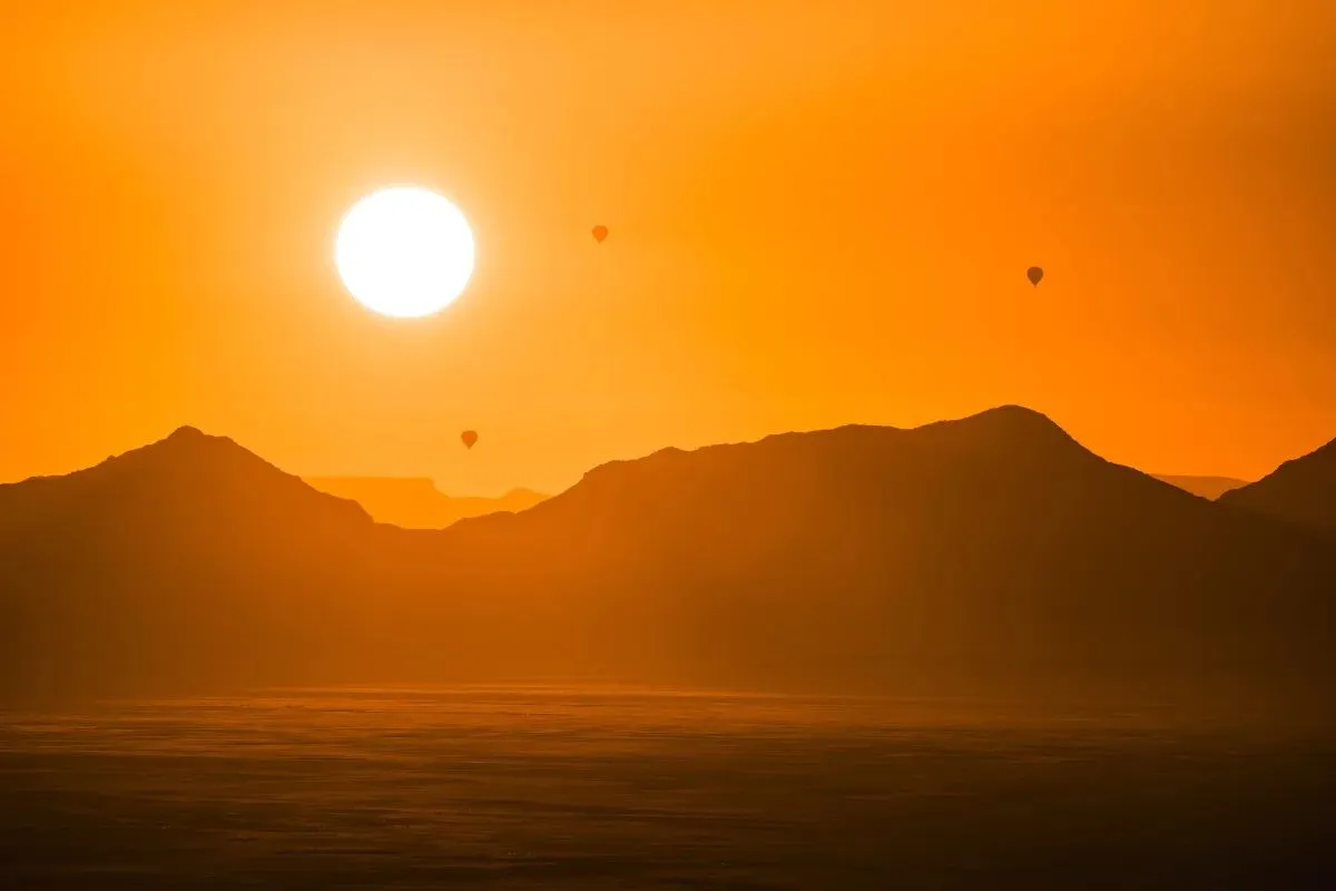 Drei Heißluftballons vor der tiefstehenden Sonne über den Bergen
