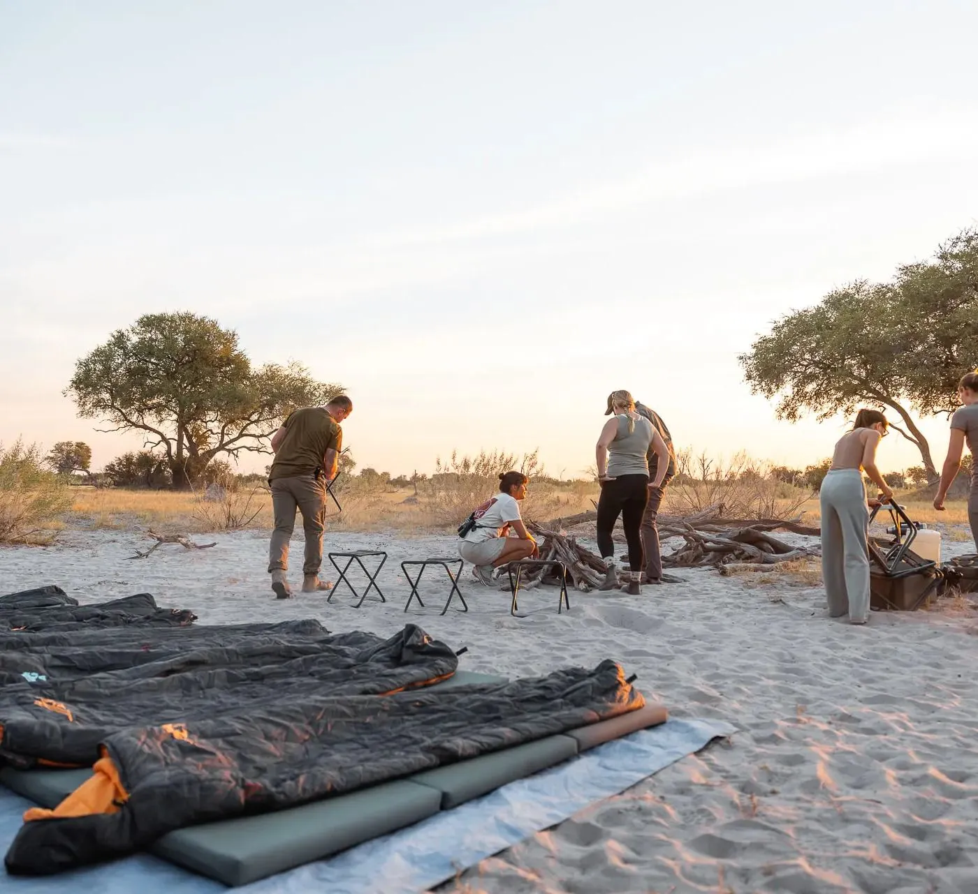 Biwak im Sand, Schlafsäcke auf Isomatten, die Gruppe richtet die Feuerstelle her