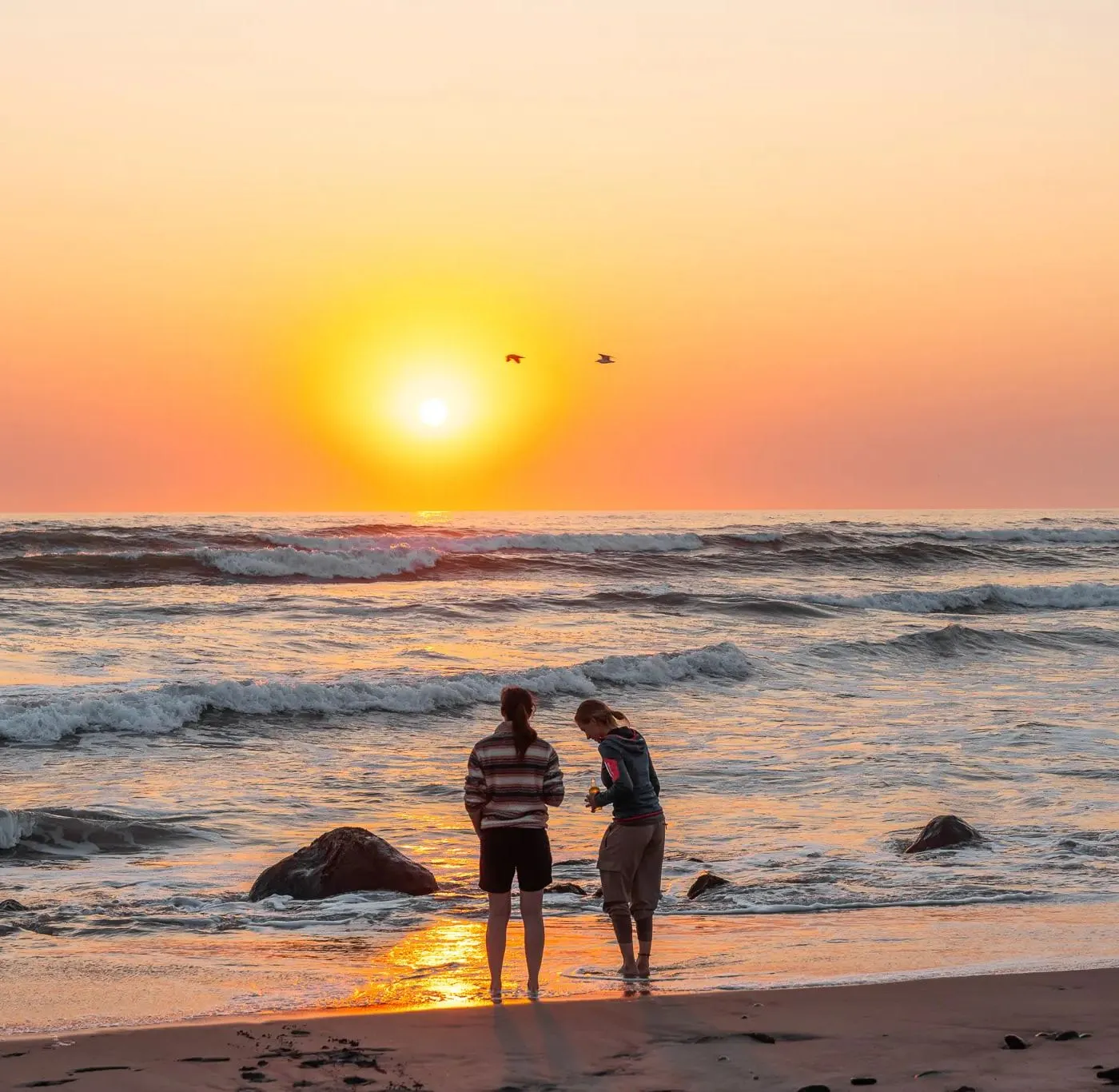 Zwei Menschen am Wasser beim Sonnenuntergang über dem Atlantik