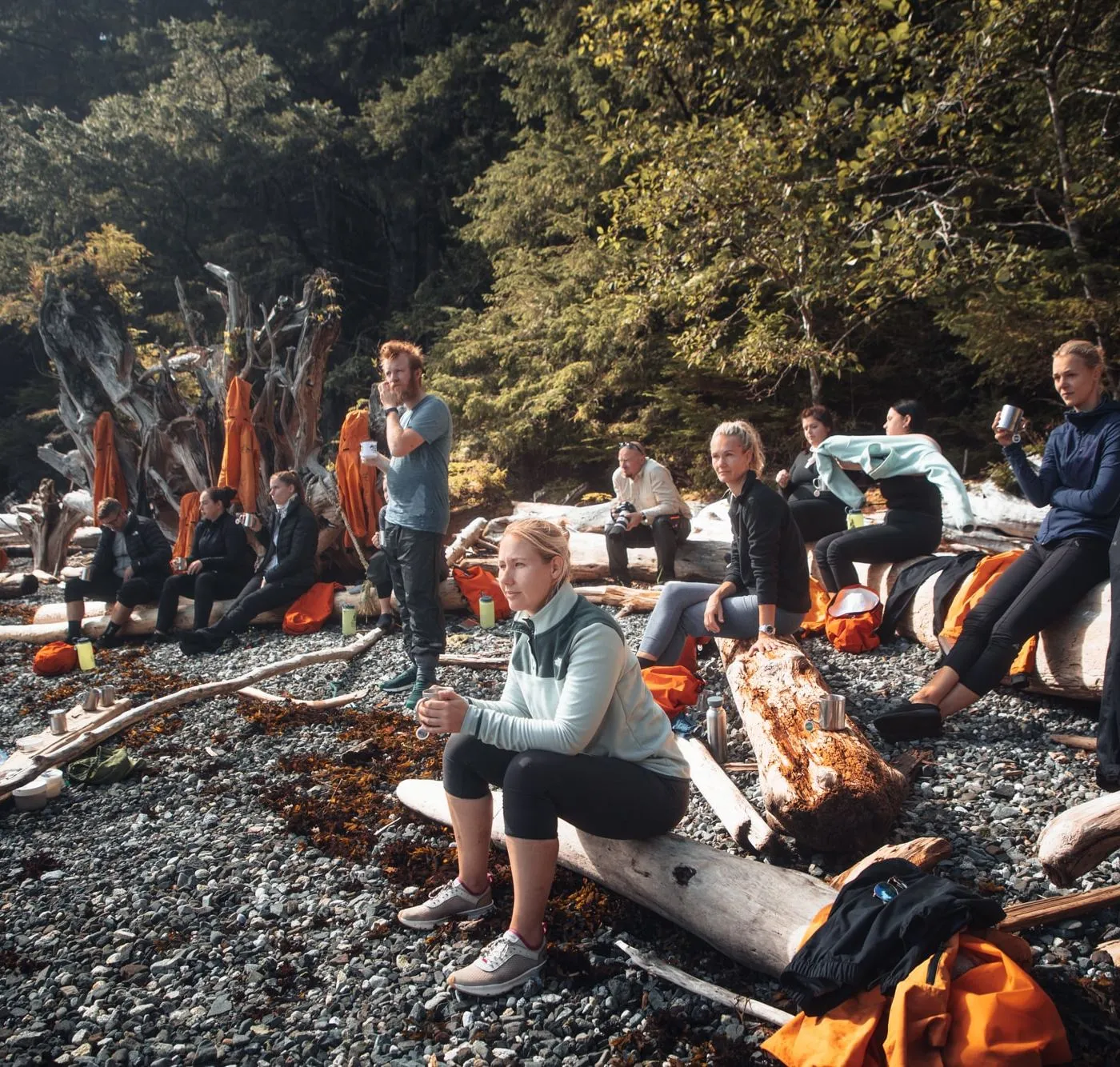 Pause am Kiesstrand, die Gruppe sitzt mit Bechern rund ums Feuer