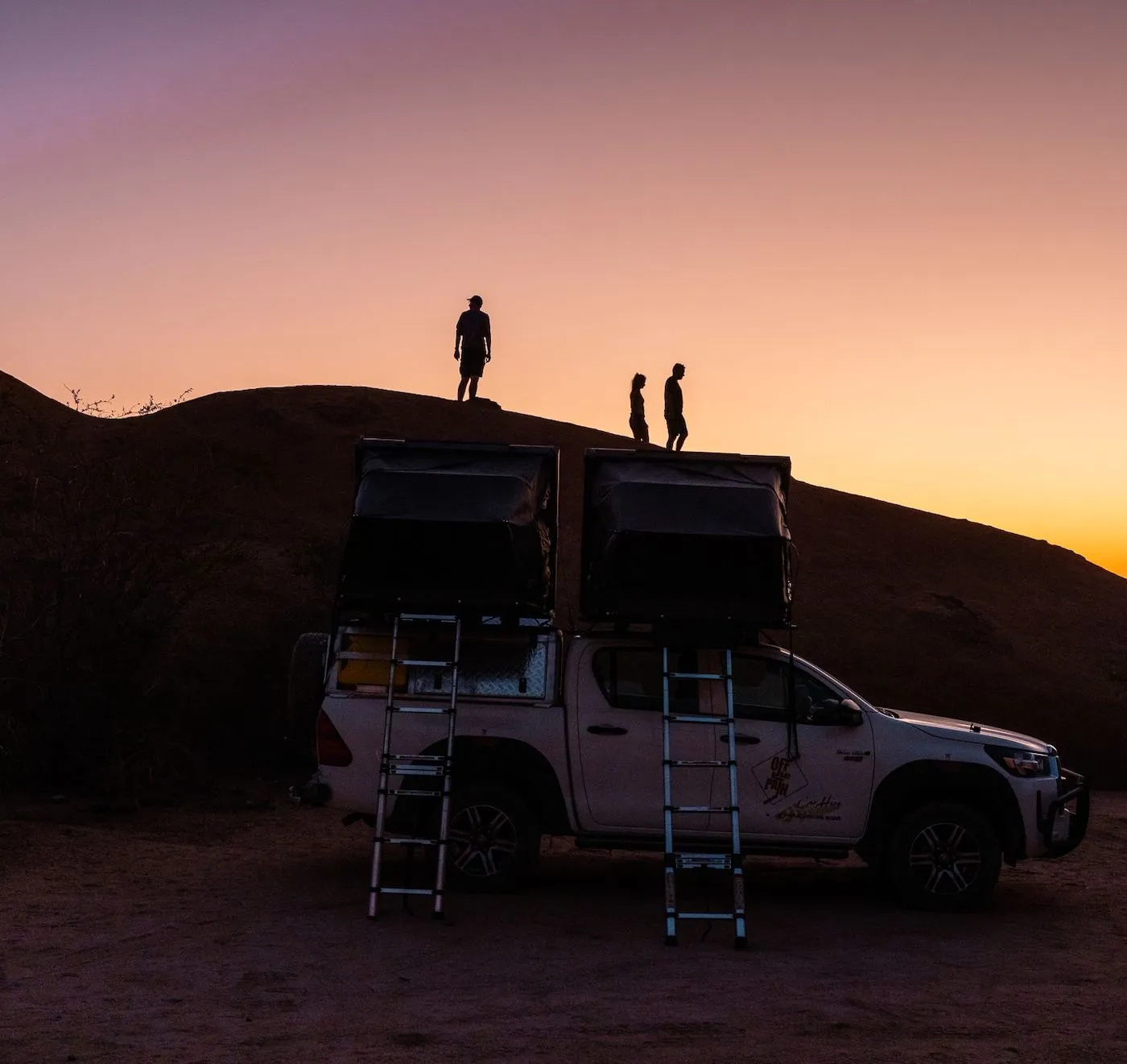 Zwei 4x4 mit Dachzelten am Fels, Gäste stehen im Abendlicht darüber