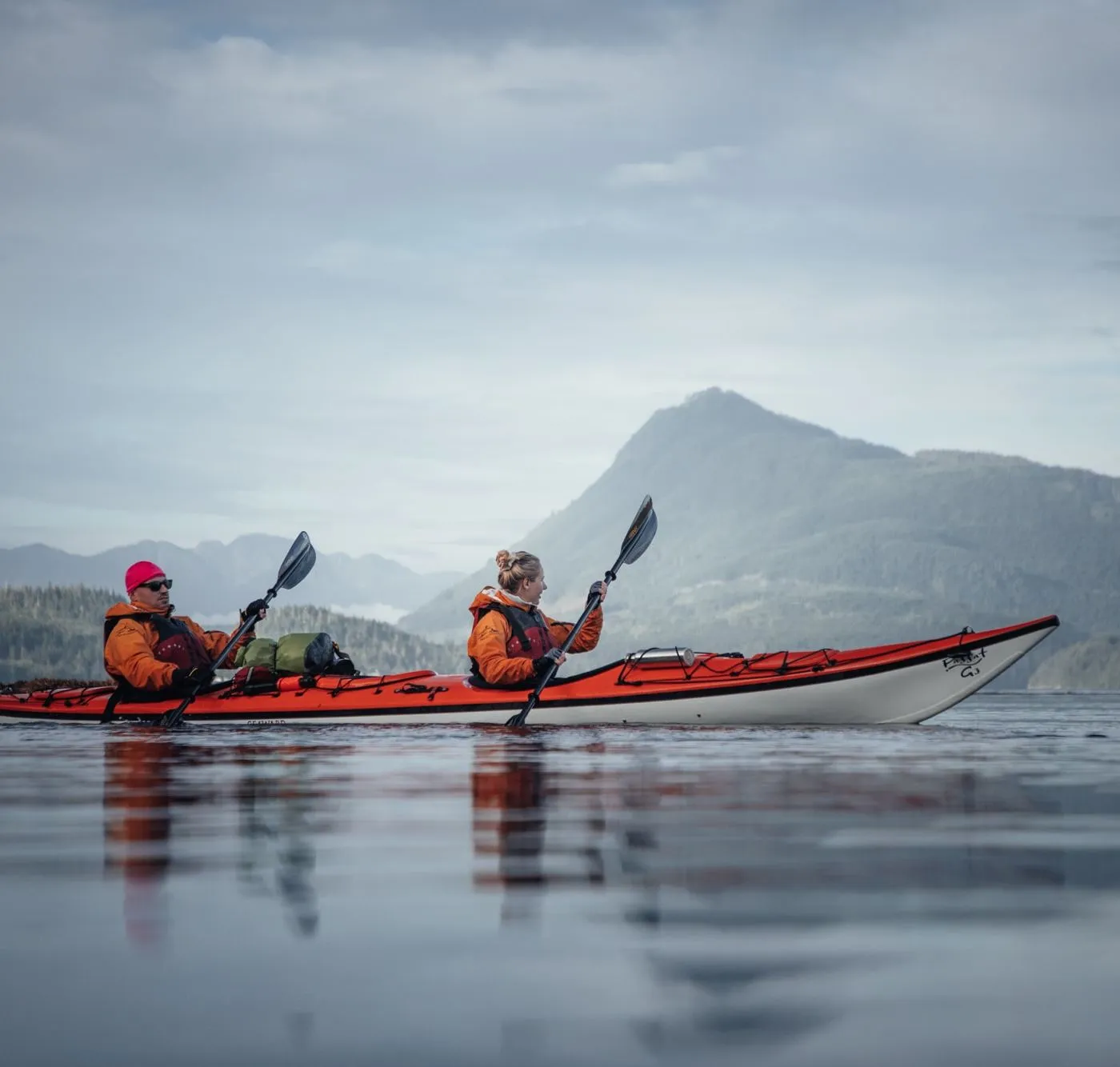 Zwei Paddler im Doppel-Kajak auf ruhigem Wasser vor einem Berg